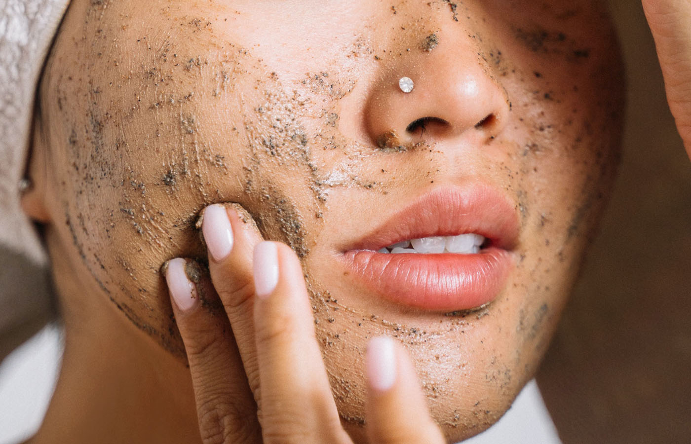 Close-up of a woman applying a facial scrub, showing textured exfoliant on her face