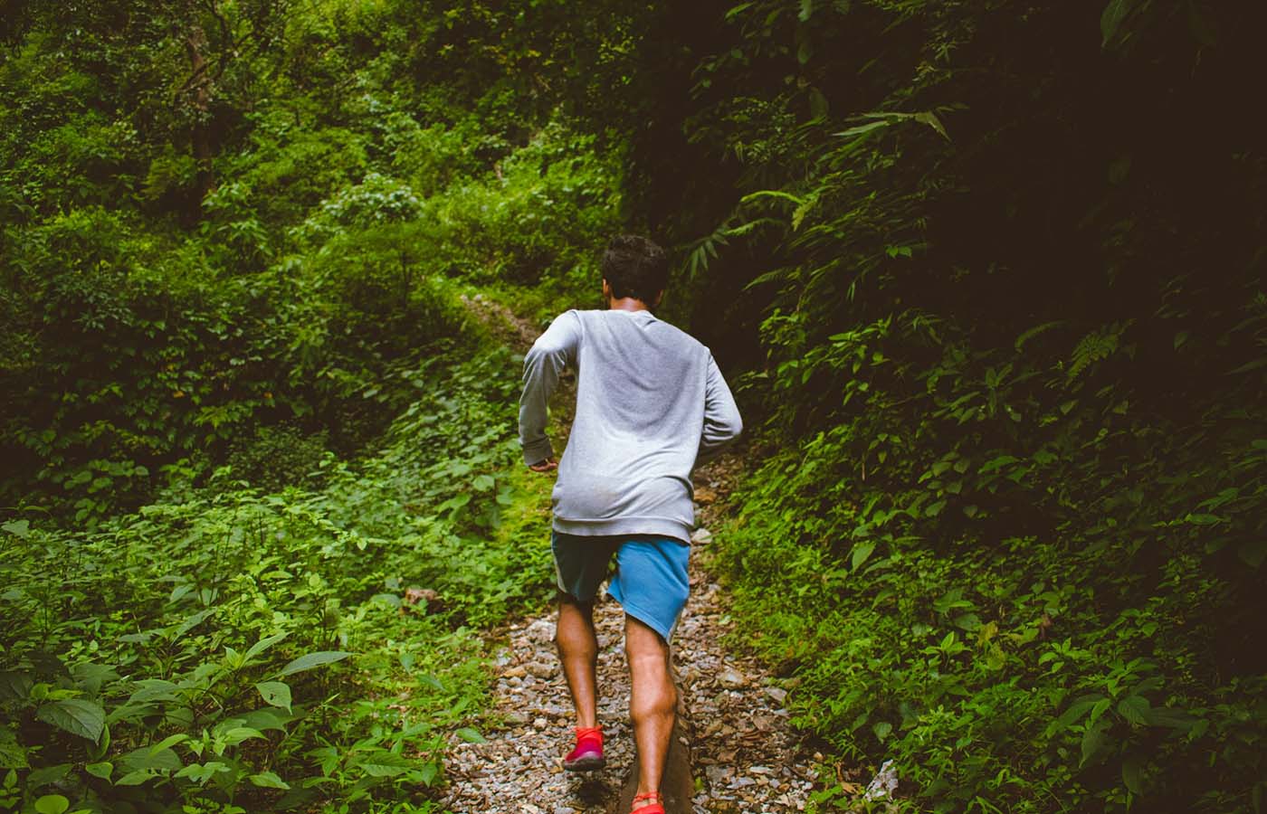 Man running uphill on a rocky forest trail surrounded by dense green foliage