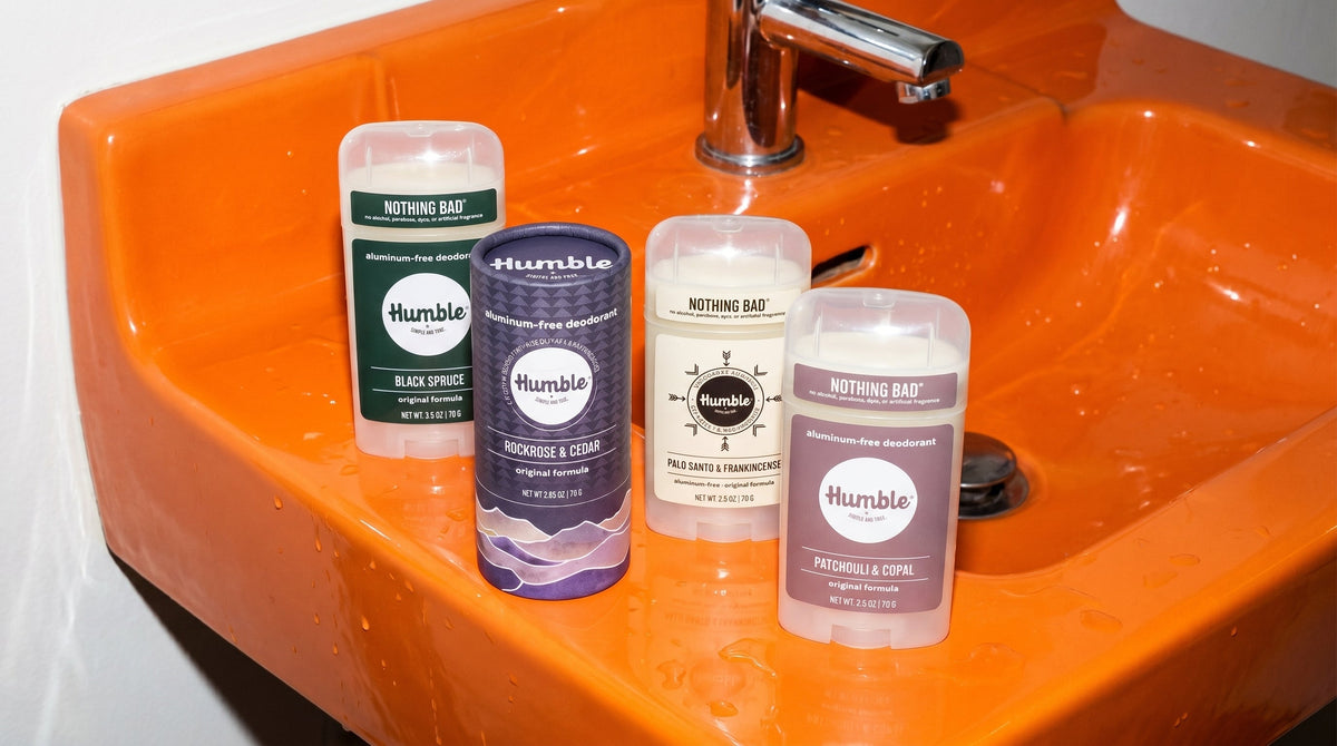 Front view of four Humble aluminum-free deodorant sticks in earthy scents on an orange sink