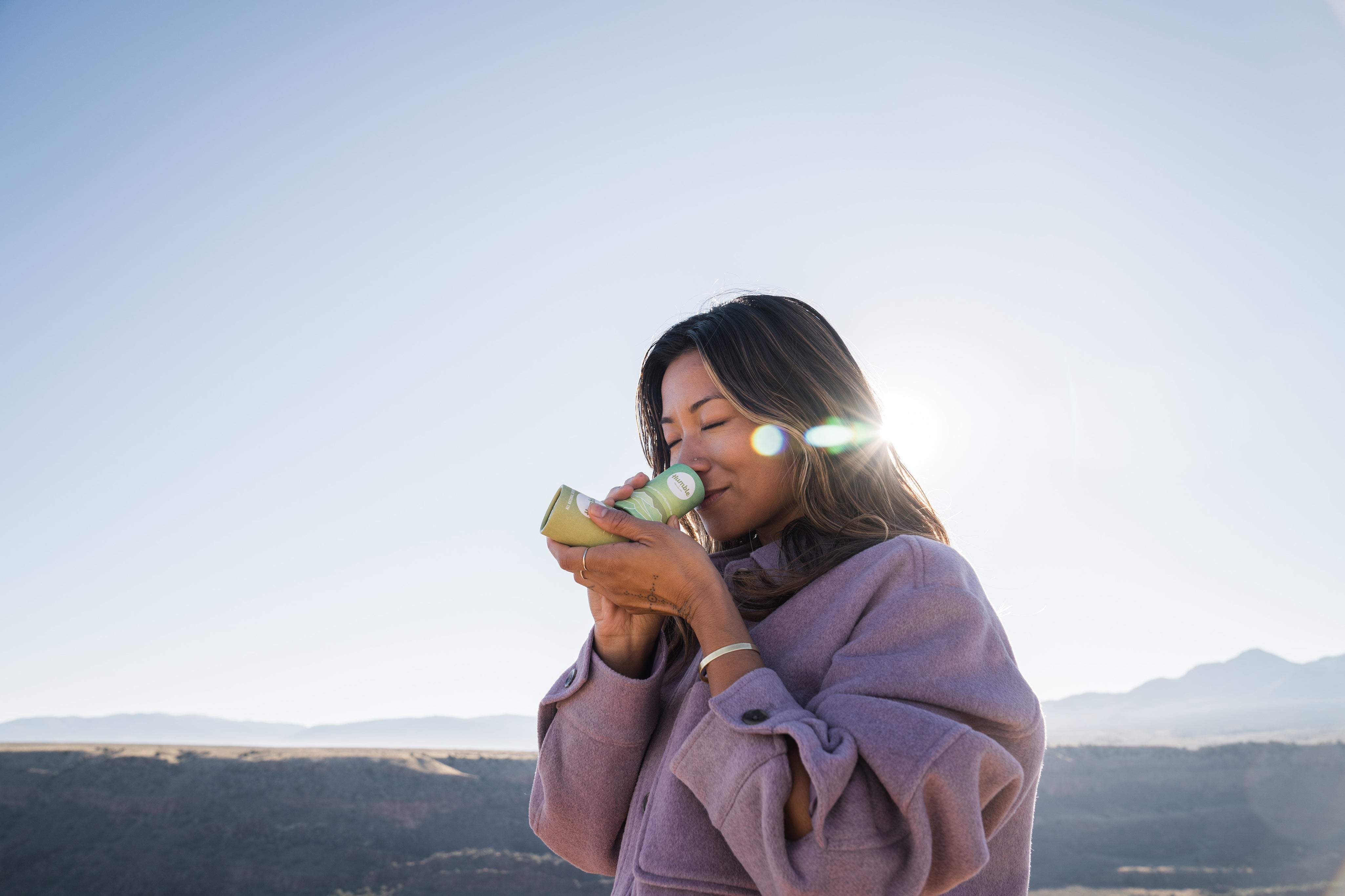 Woman smelling paperboard deodorant with blue sky in background