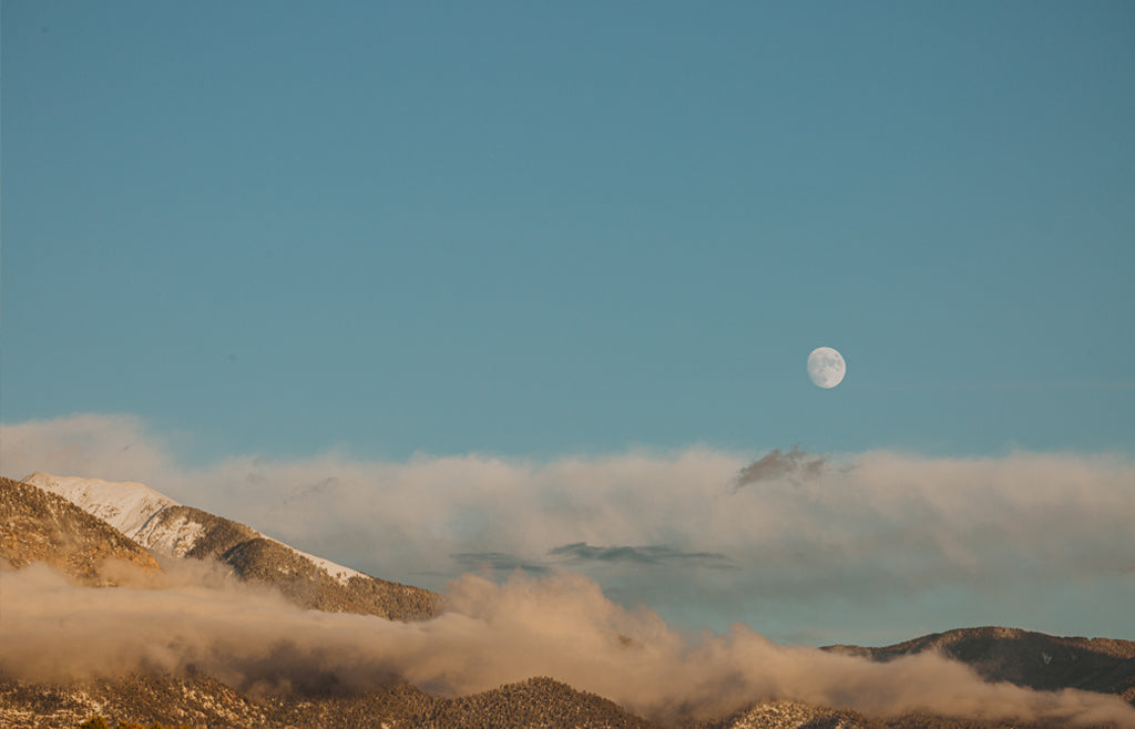 Moon low in the blue daytime sky over mountains