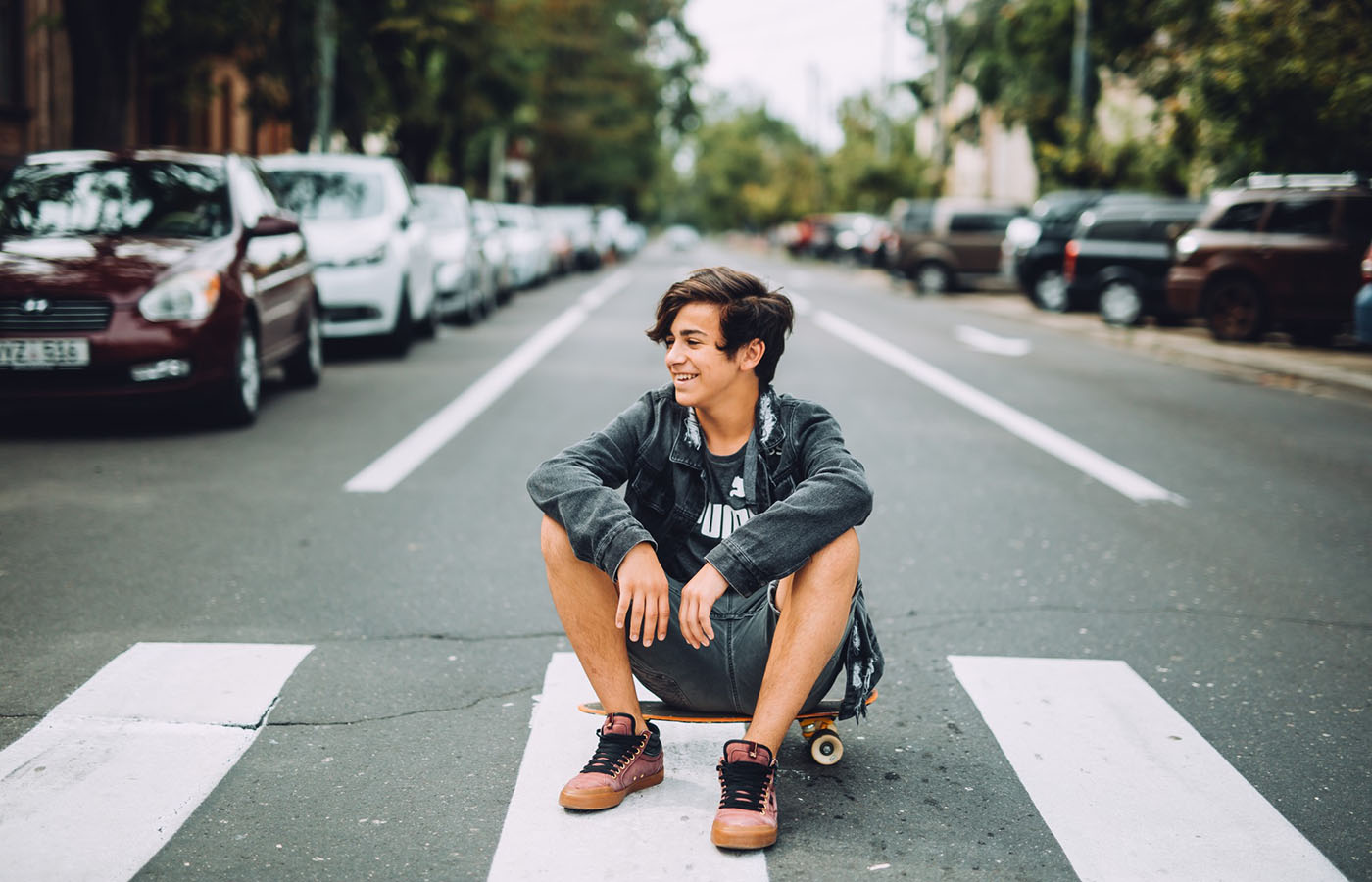 Boy sitting on skateboard in crosswalk