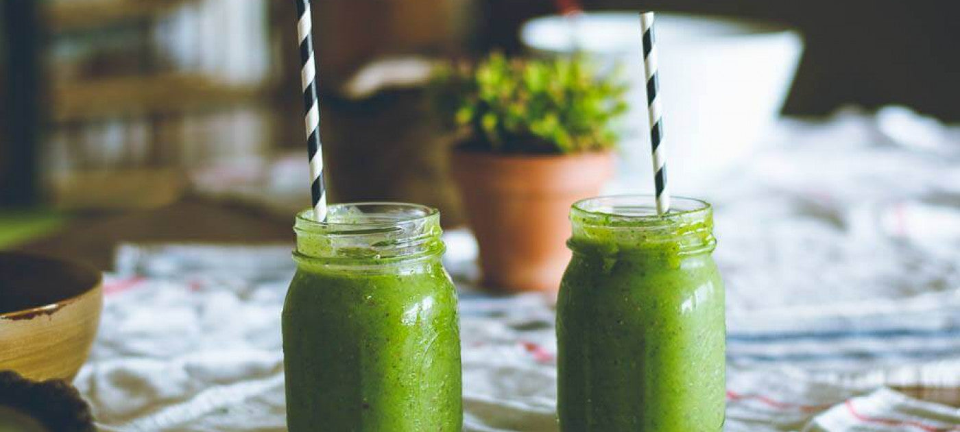 Two green smoothies with paper straws on a table