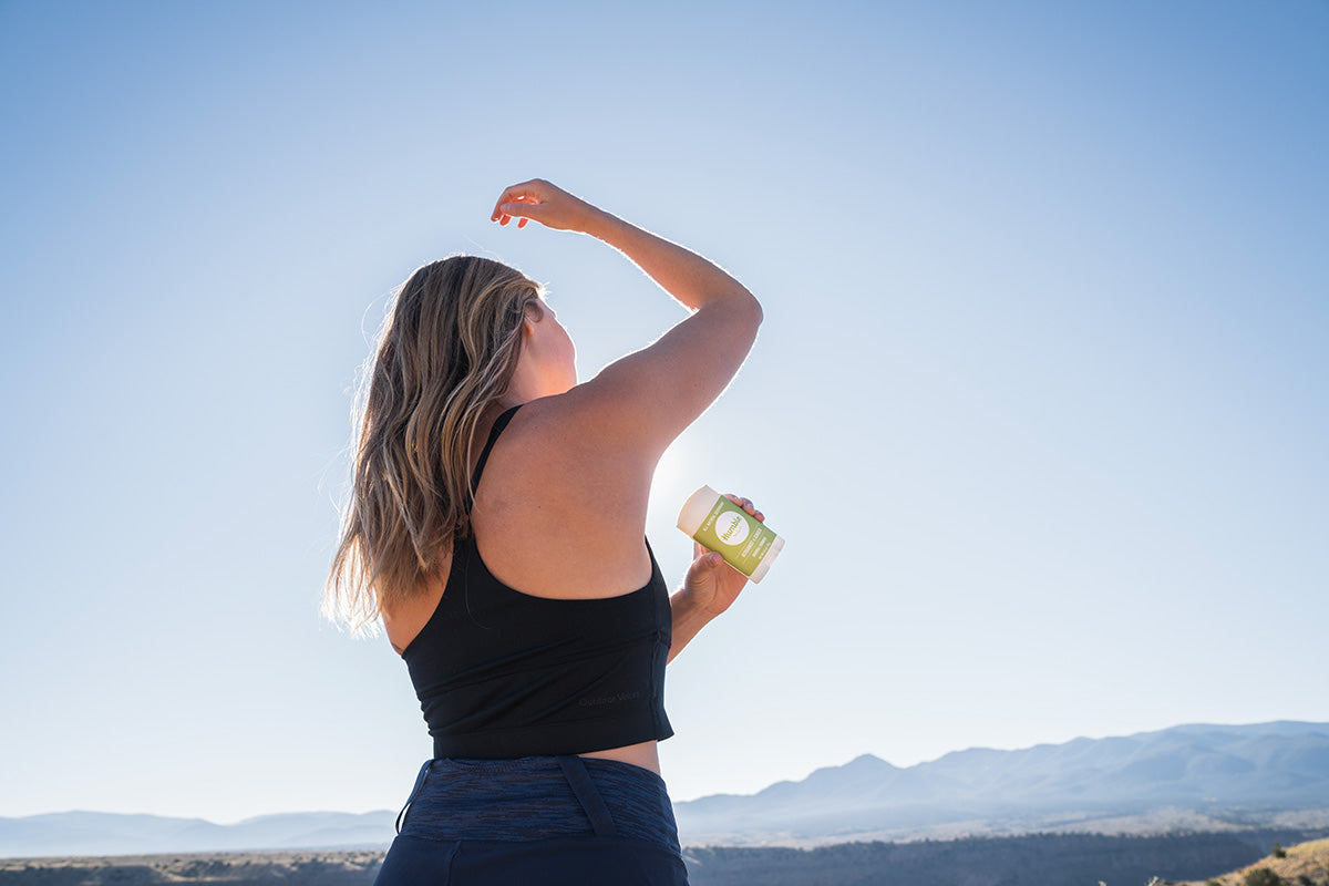Woman applying deodorant to underarm outdoors