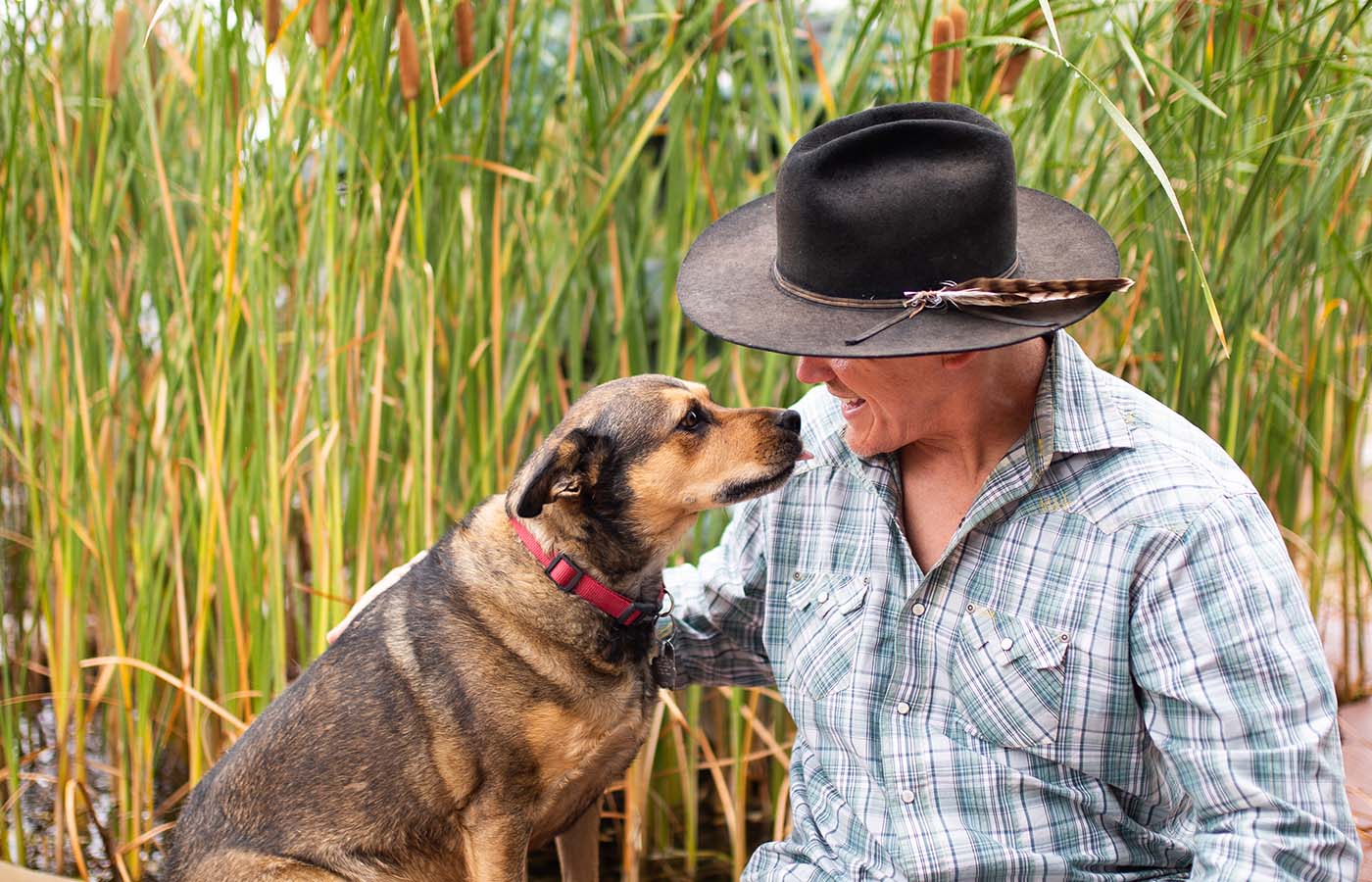 Man in hat looking at dog with tall grasses in the background