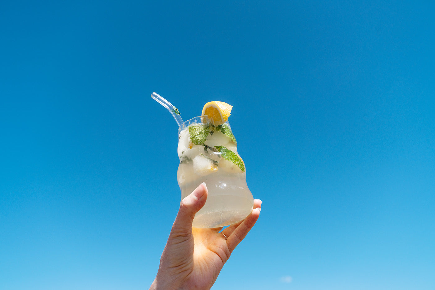 Hand holding glass of rosemary mint refresher in the blue sky