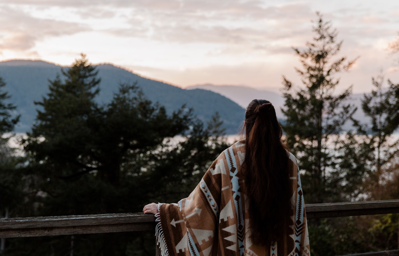 Woman in poncho on balcony staring at a water view