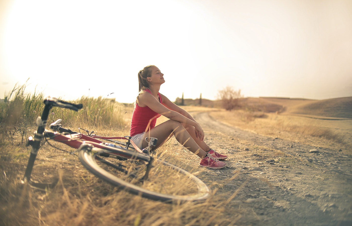 Woman sitting on gravel path next to red bike lying on the ground