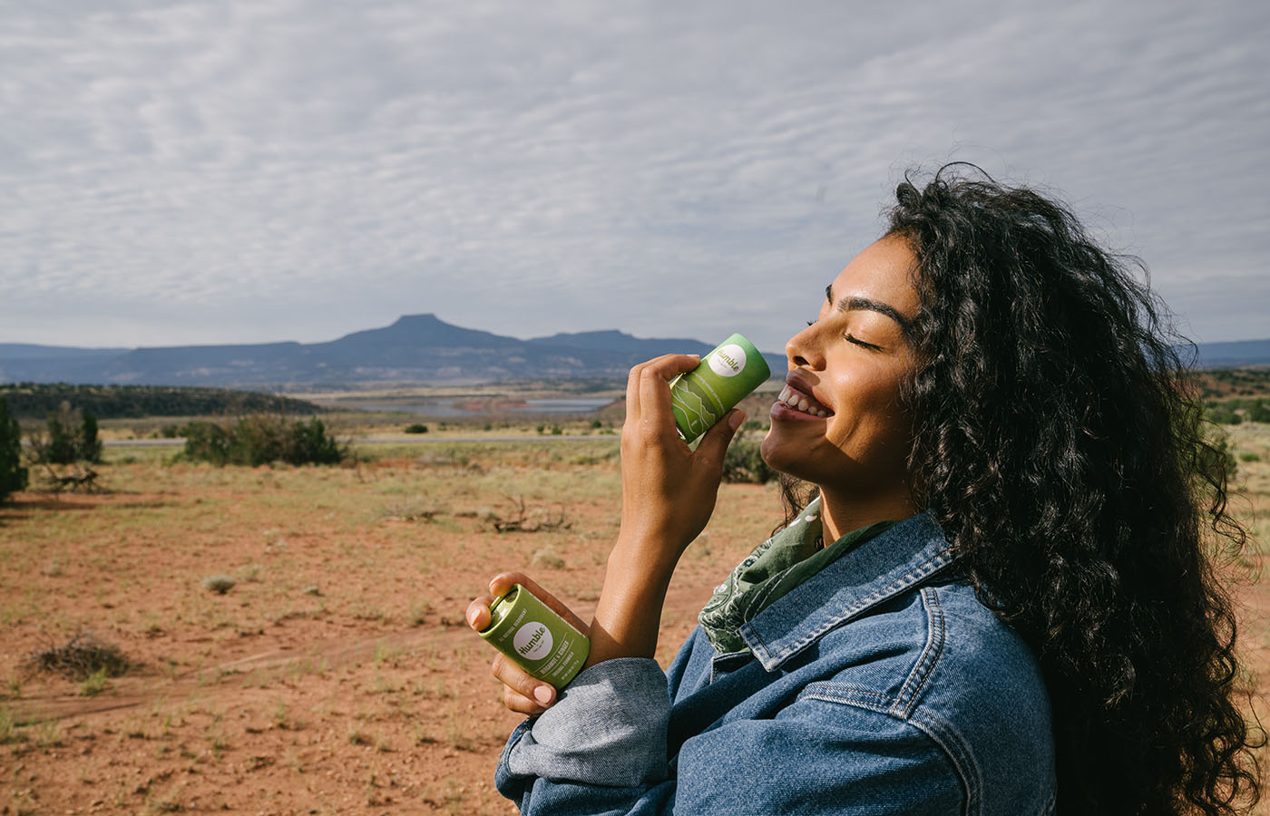 Young woman in the desert holding paperboard deodorant and smelling one