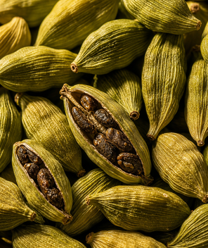 Close-up of green cardamom pods with one open showing brown seeds.