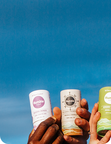 Five colorful skincare bottles held by people against a blue sky.