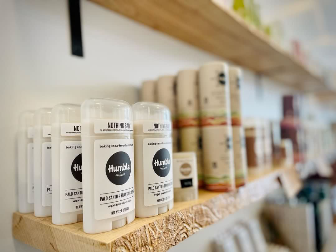 Angled close-up of Humble deodorant sticks in white push-up tubes on a wooden store shelf