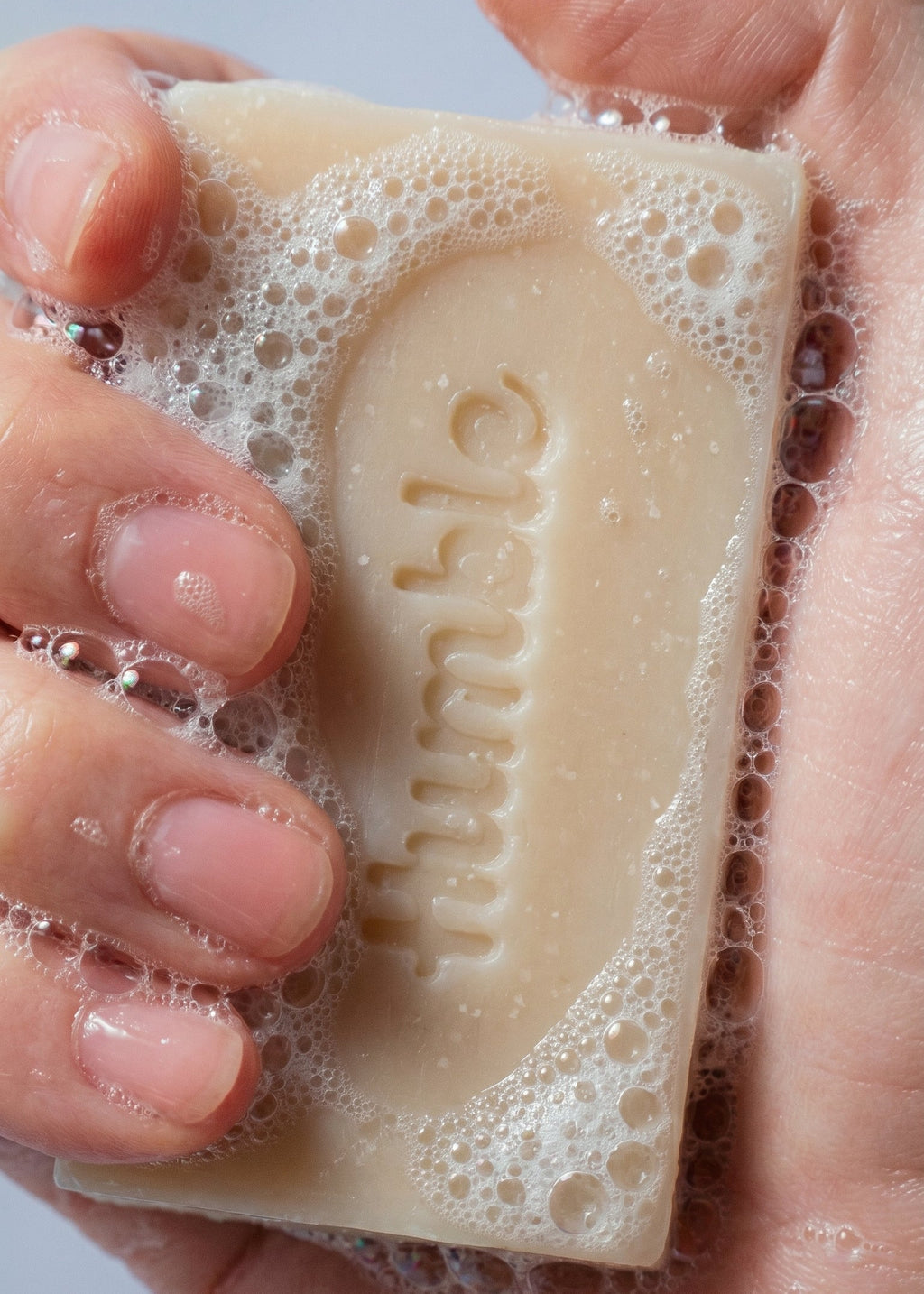 Close-up of Mountain Lavender Natural Bar Soap held in hands, lathered and showing the embossed Humble logo against a light background