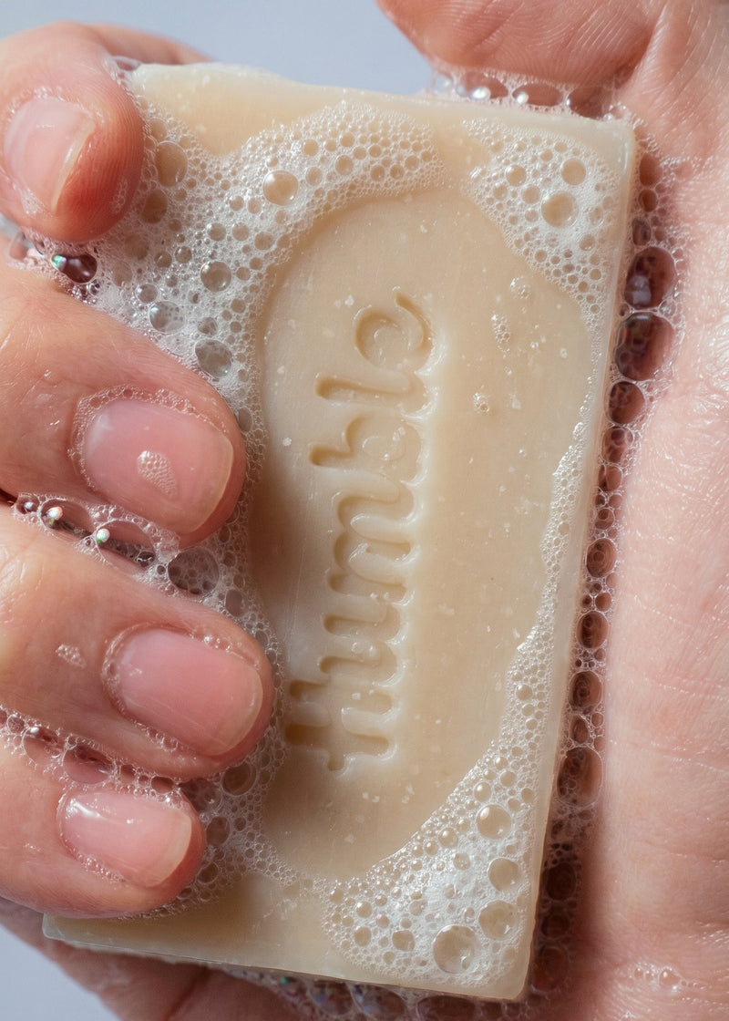 Close-up of Mountain Lavender Natural Bar Soap held in hands, lathered and showing the embossed Humble logo against a light background