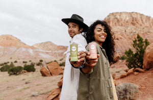 two people standing back to back in the desert holding out sticks of deodorant