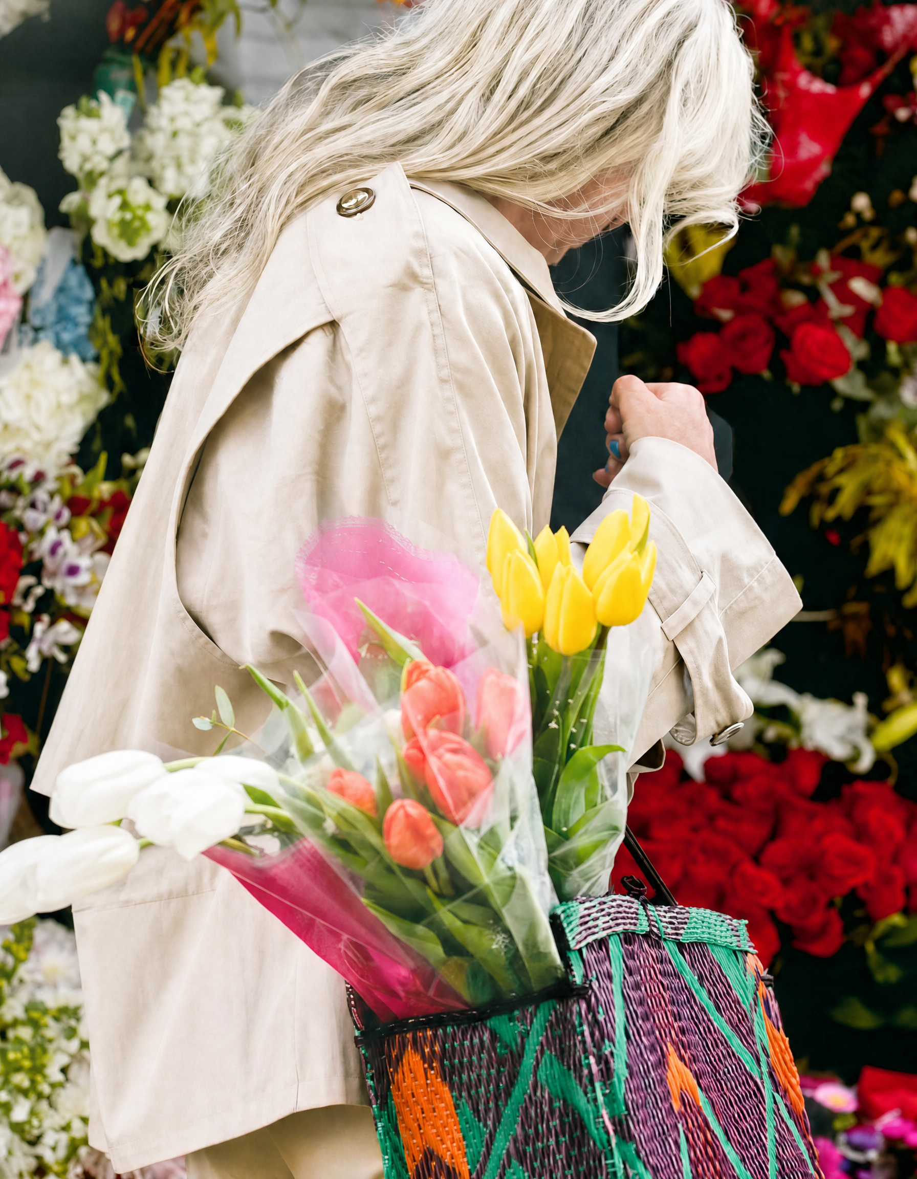 Person holding a bouquet of tulips with a colorful bag against a floral background