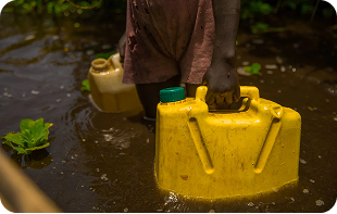 Person carrying yellow water containers through waterlogged terrain