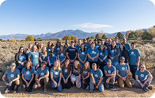 Group of people wearing matching blue shirts in a desert landscape with mountains in the background.