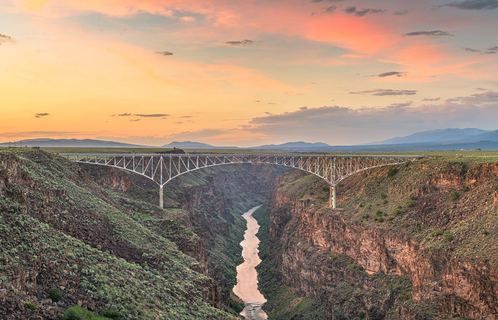 Rio Grande Gorge Bridge spanning a deep canyon at sunset with the river winding below and distant mountains