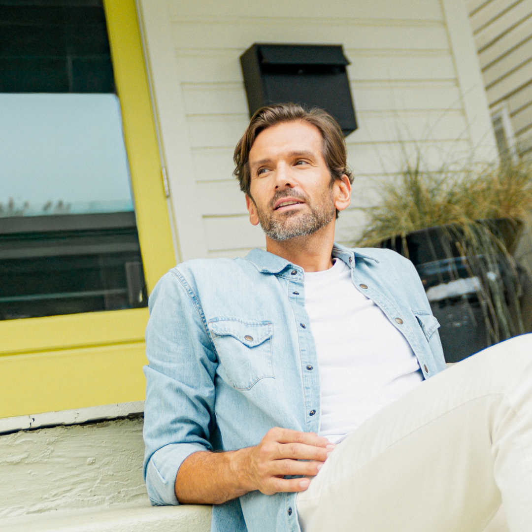 A man in a denim shirt sitting outside on a porch step