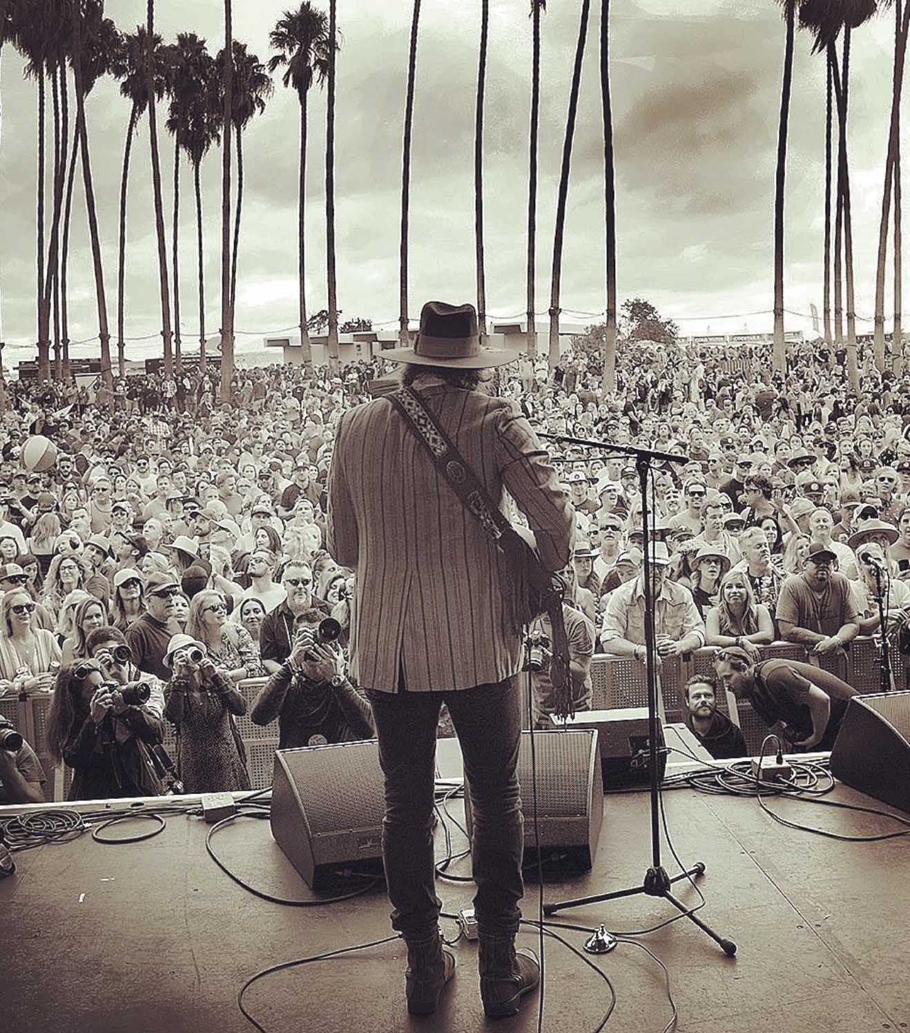 man playing music on stage to a crowd in black and white 