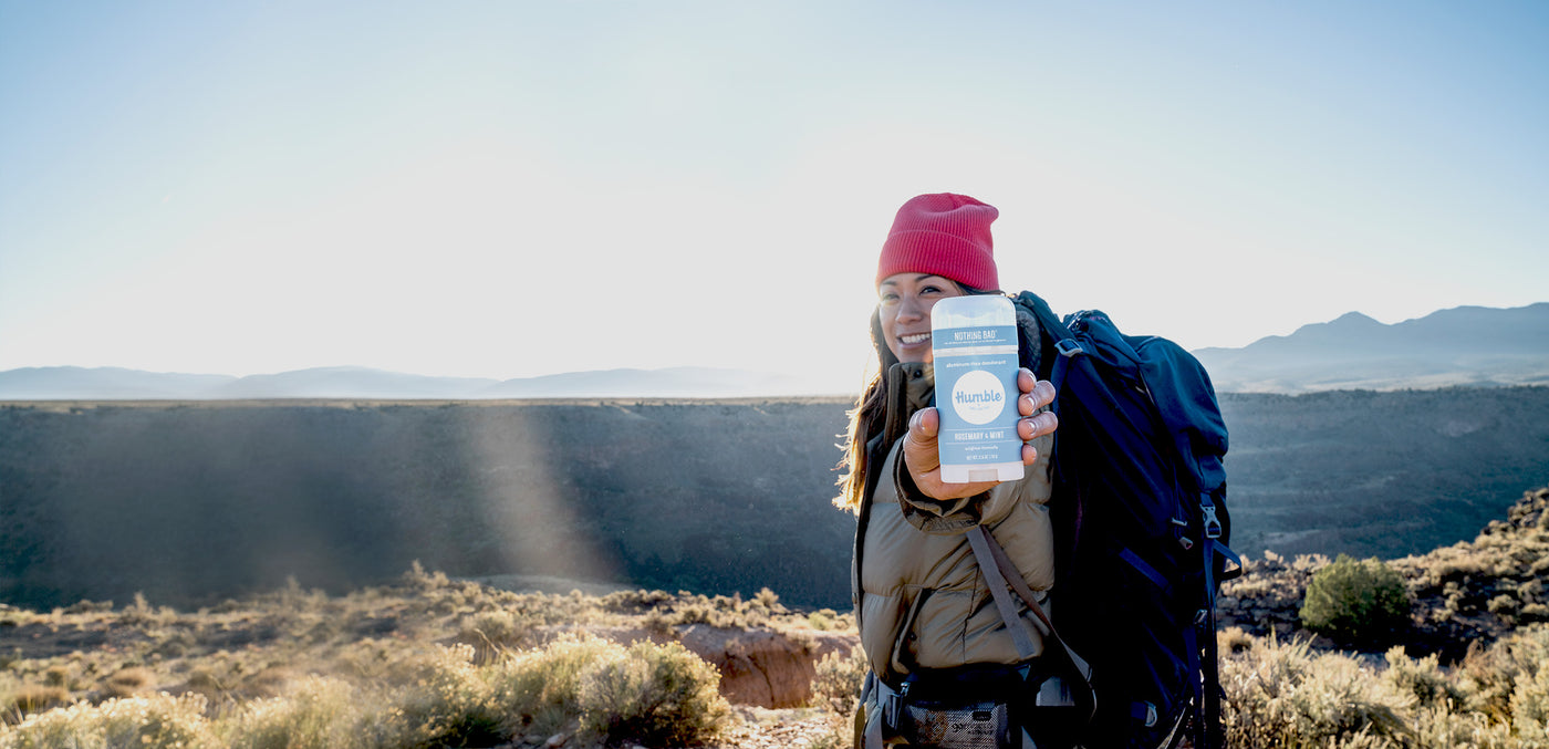 A smiling woman backpacking in the desert holding a deodorant