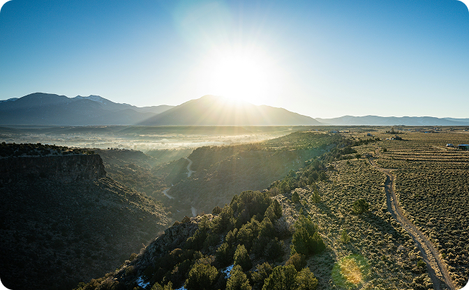 Scenic view of a mountain range with a clear blue sky and sun.
