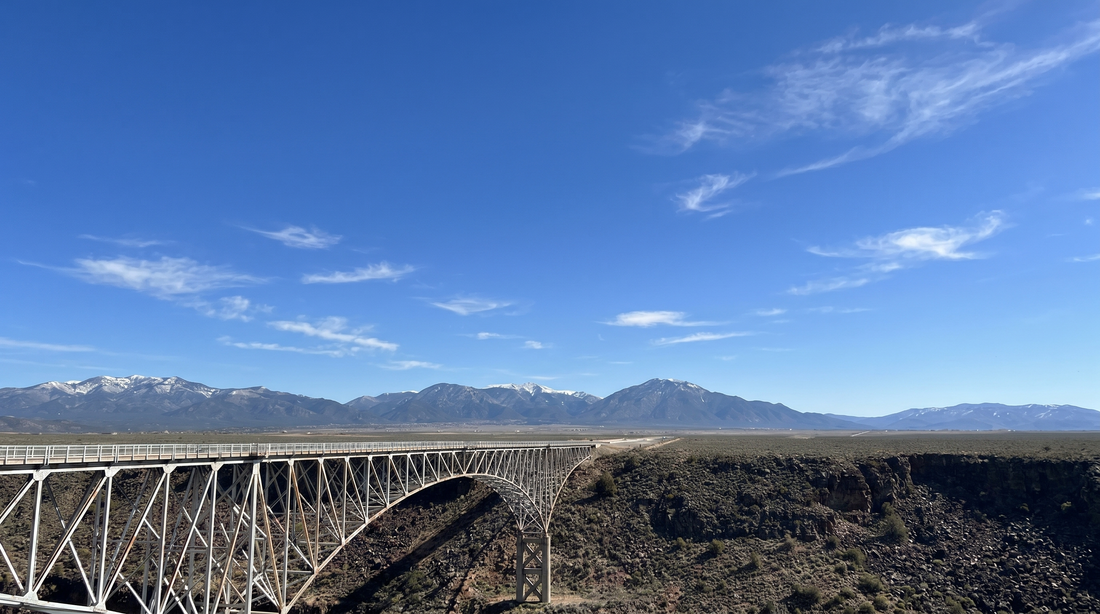 Bridge over a canyon with mountains in the background under a clear blue sky.