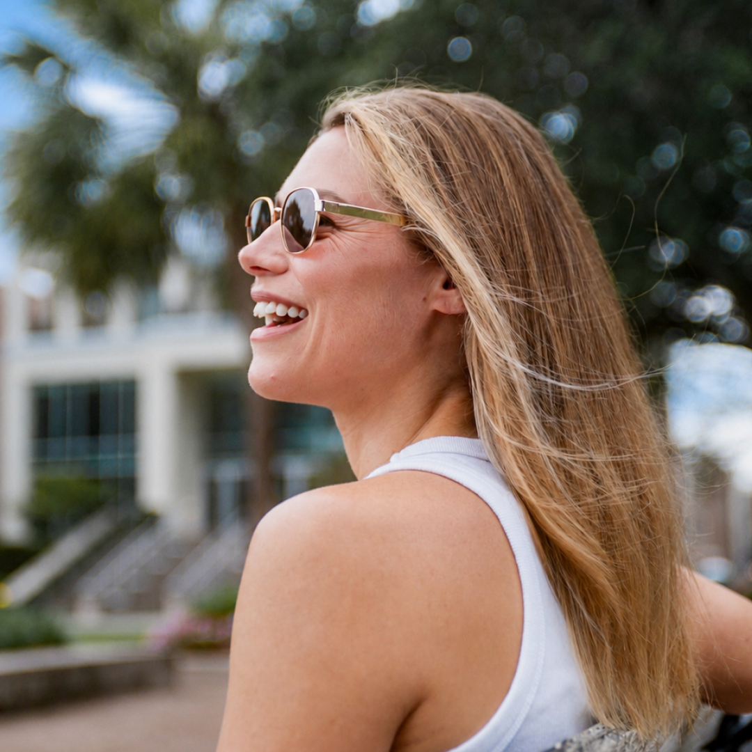 A woman with long blonde hair and sunglasses laughing outdoors
