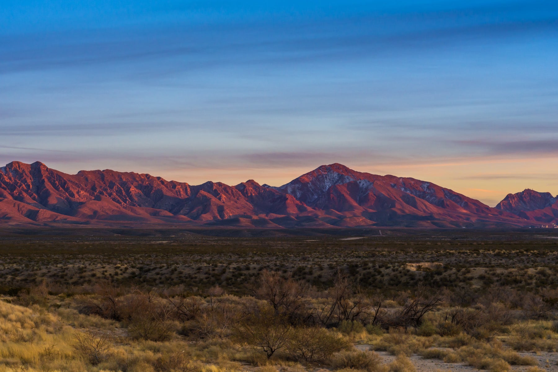 a sunset falls on a desert landscape with mountains in the distance 