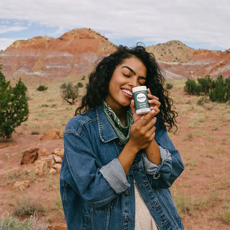 a woman smelling deodorant outside in the desert 